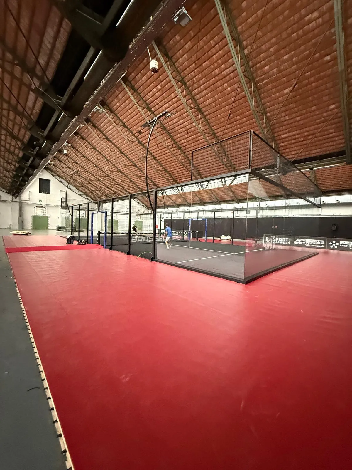Pista de pádel con superficie roja y estructura de techo de ladrillo